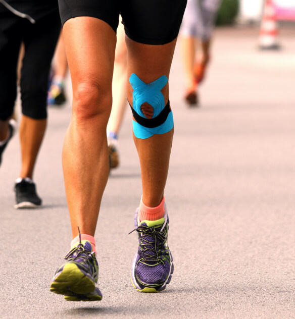 The legs of a runner during a race on a street with blue tape applied to their left knee